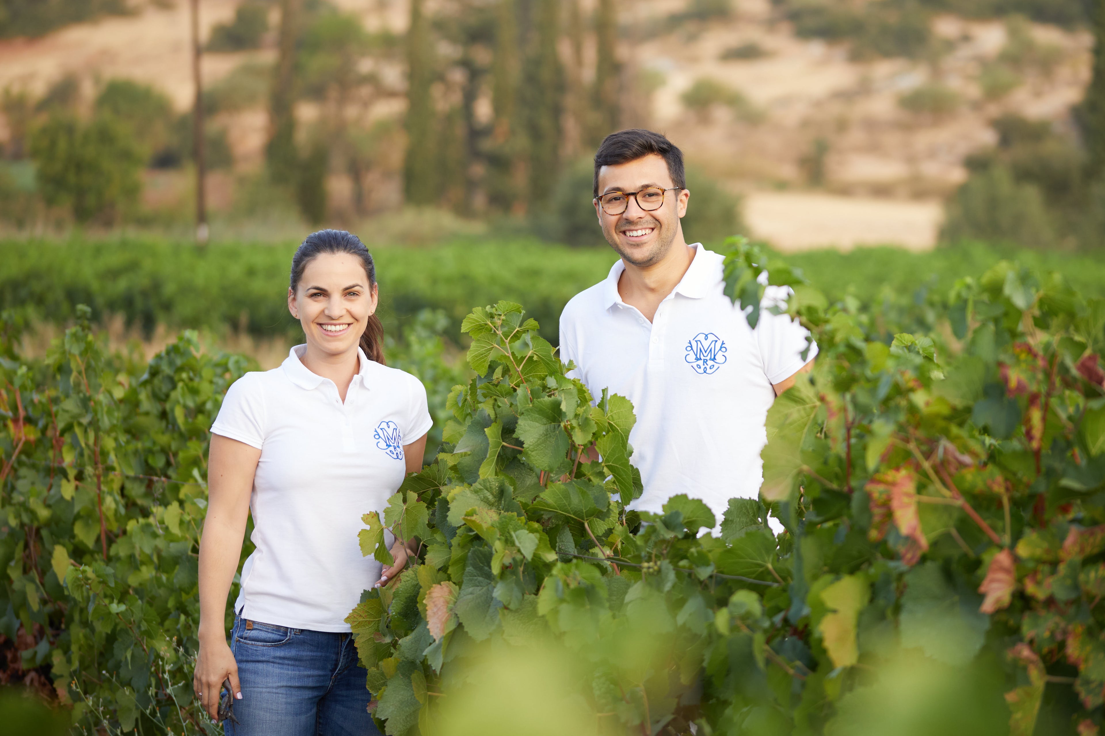 Two people in white polo shirts standing in a vineyard